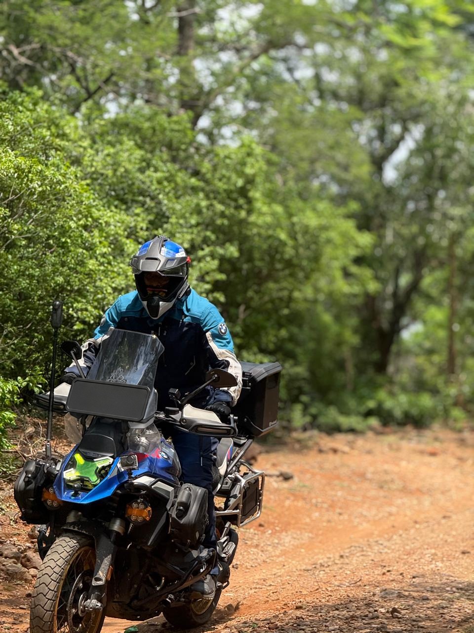 Rider on a blue BMW R1300GS exploring a forest dirt road
